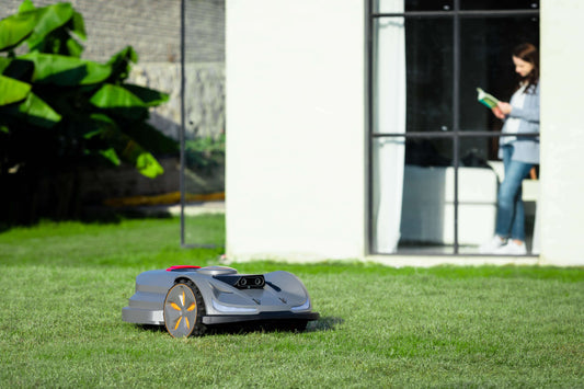 SunSeeker Orion X7 robotic lawn mower efficiently mowing grass in a stylish backyard with a woman reading nearby.
